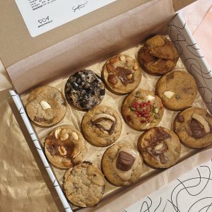 Coffret de 12 cookies artisanaux Sweet Notes aux saveurs variées : chocolat, noisettes, spéculoos, framboises et Oreo, présentés dans une boîte en carton.
