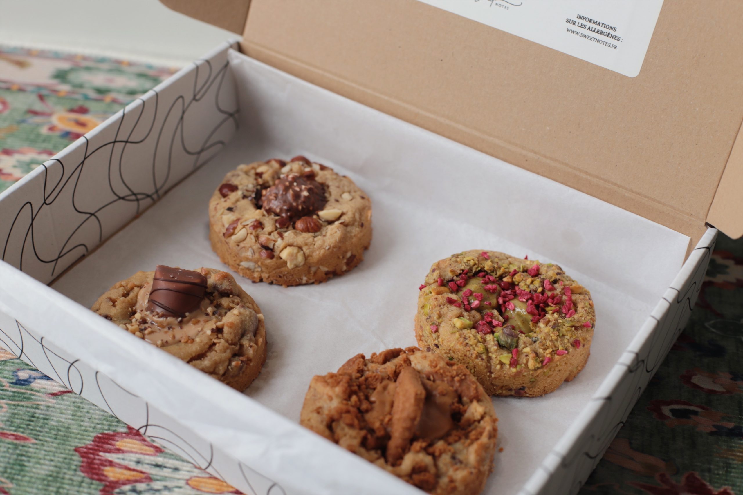 Coffret en carton Sweet Notes contenant quatre cookies artisanaux garnis de noisettes, chocolat, framboises séchées et spéculoos.