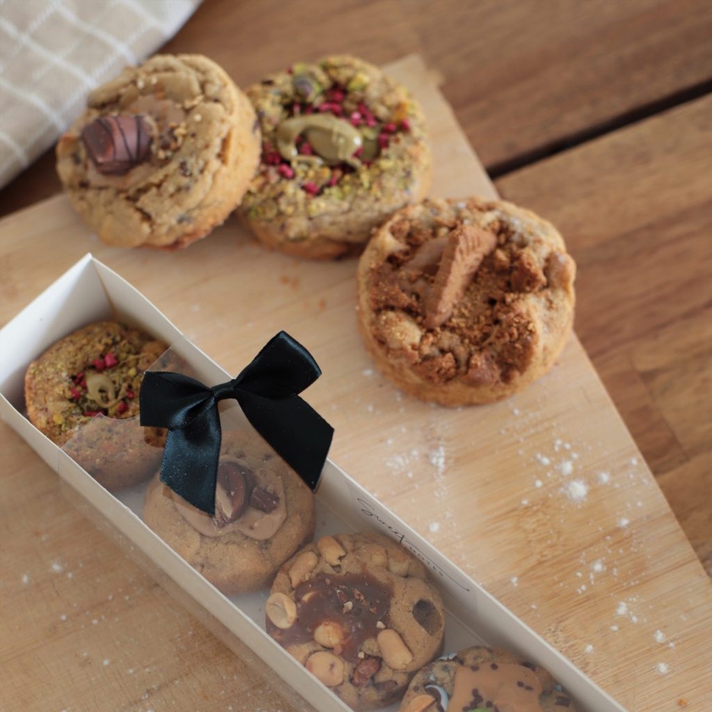 Coffret cadeau Sweet Notes avec cookies artisanaux variés, décoré d’un ruban noir, accompagné de cookies disposés sur une planche en bois